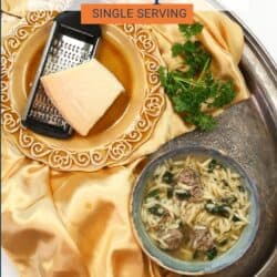 a bowl of Italian Wedding Soup on a silver tray next to a gold napkin and parmesan cheese.