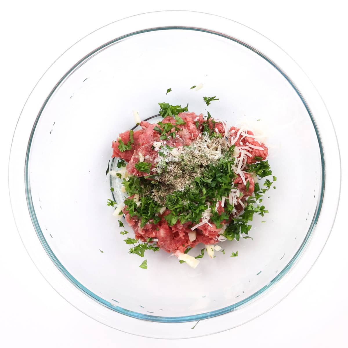 a bowl filled with ground beef, parsley, seasonings, and garlic.