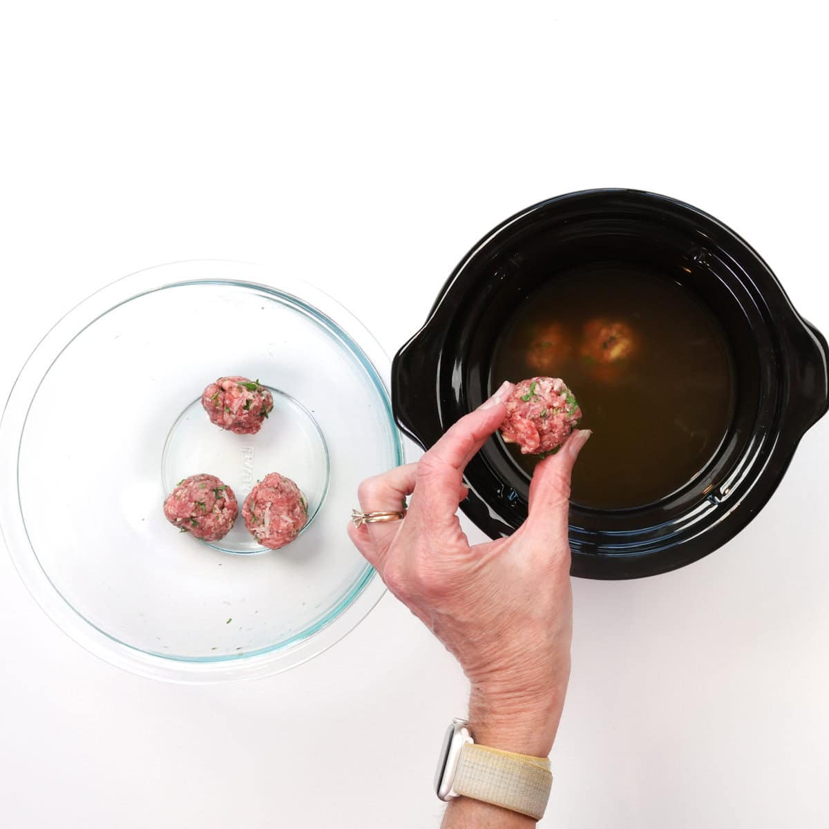 a hand placing meatballs into a slow cooker.