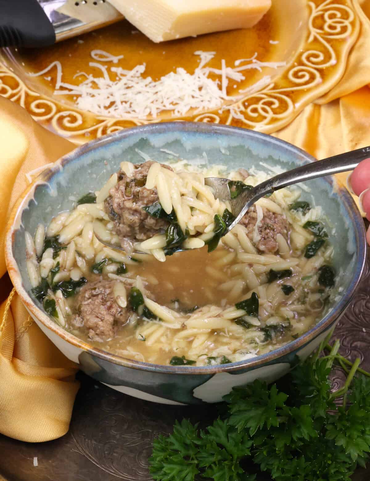 a meatball on a spoon above a bowl of Italian Wedding Soup.