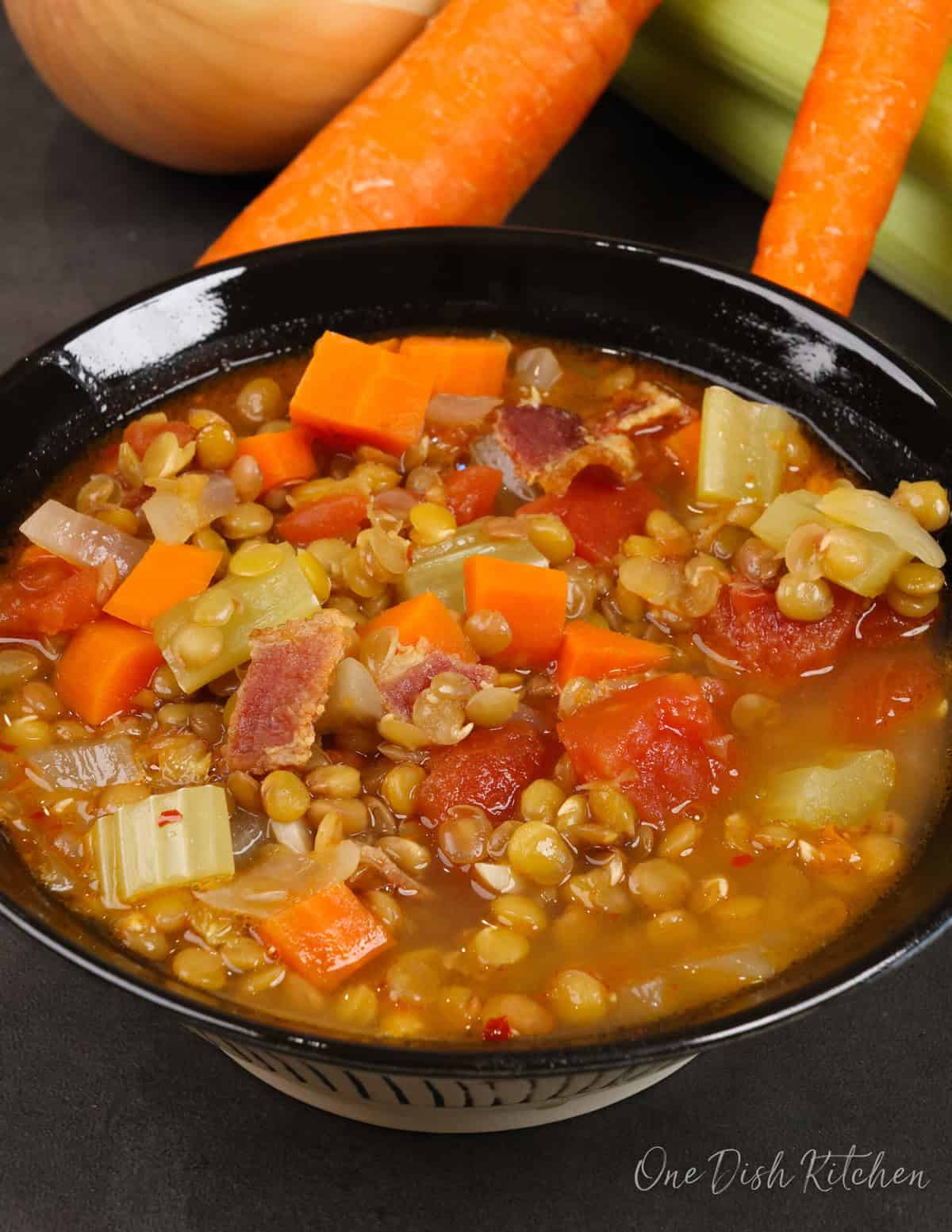 a bowl of lentil soup next to carrots, celery, and onions.