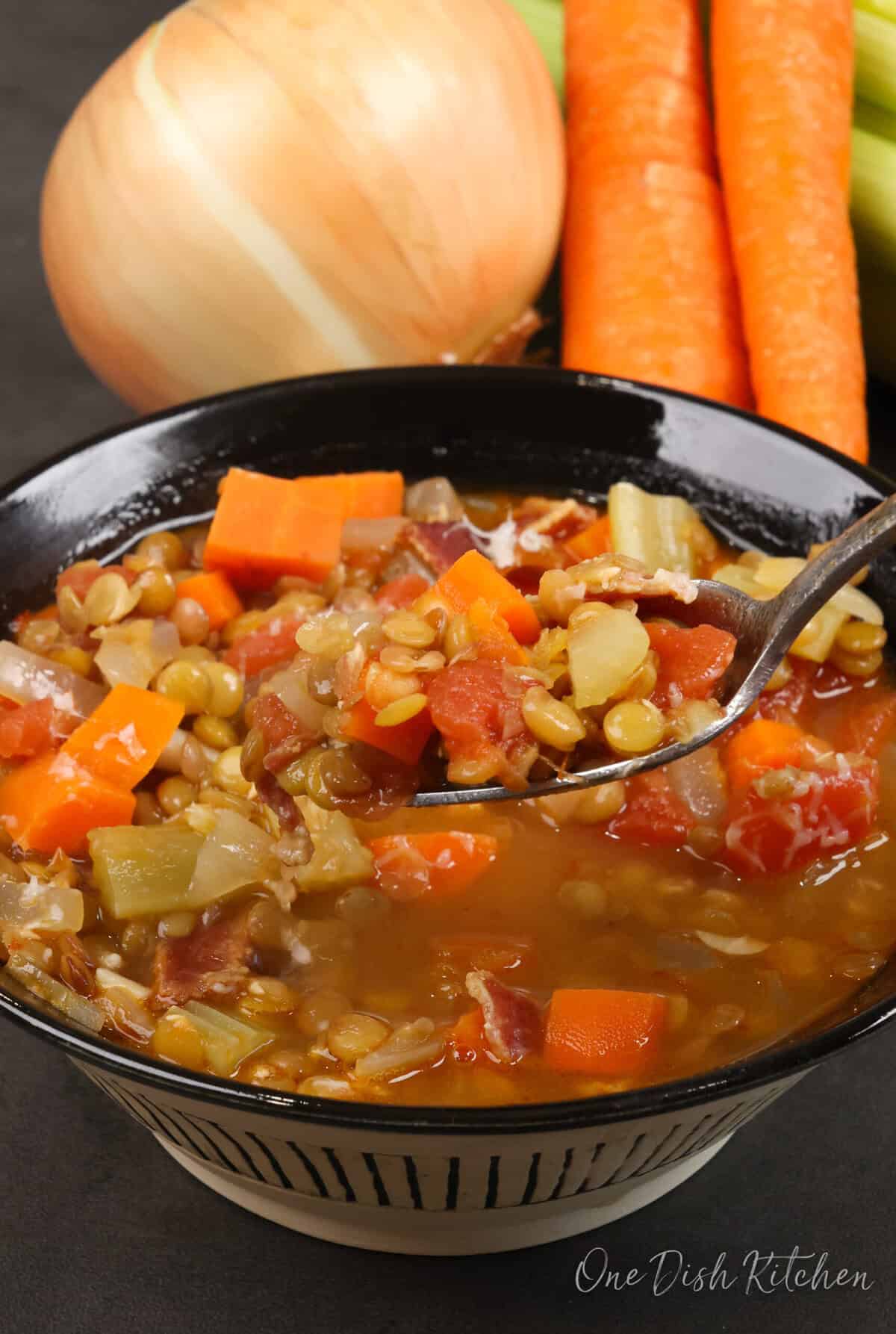 a bowl of lentil soup with a spoon filled with lentils and tomatoes above the bowl.