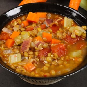 a bowl of lentil soup next to carrots, celery, and onions.