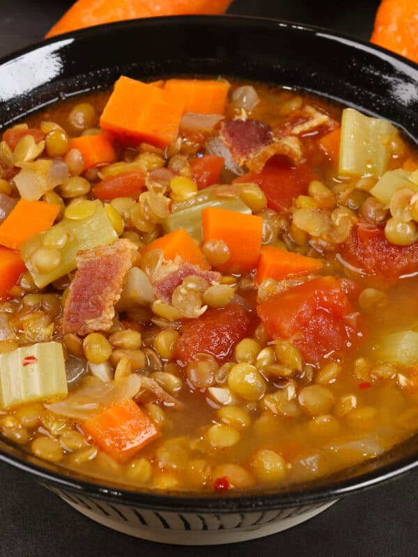 a bowl of lentil soup next to carrots, celery, and onions.