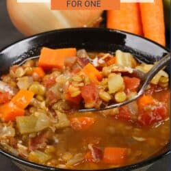 a bowl of lentil soup with a spoon filled with lentils and tomatoes above the bowl.