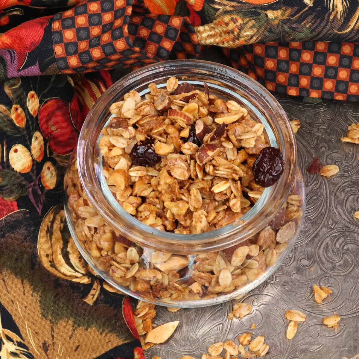 maple granola in a jar on a silver tray next to an orange and black napkin.