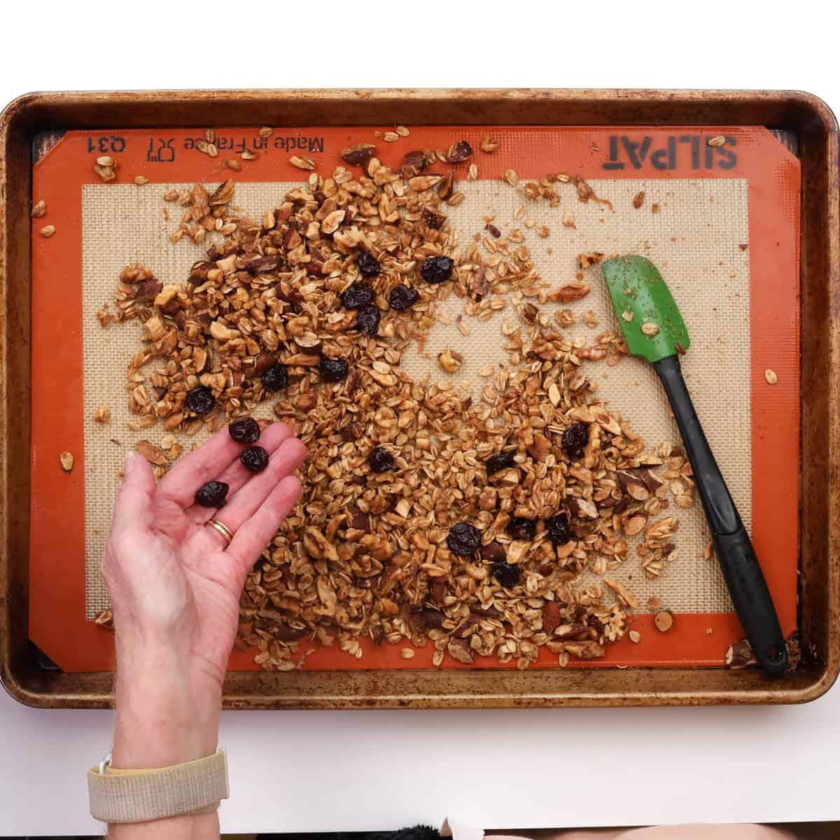 mixing dried fruit into baked granola on a baking sheet.