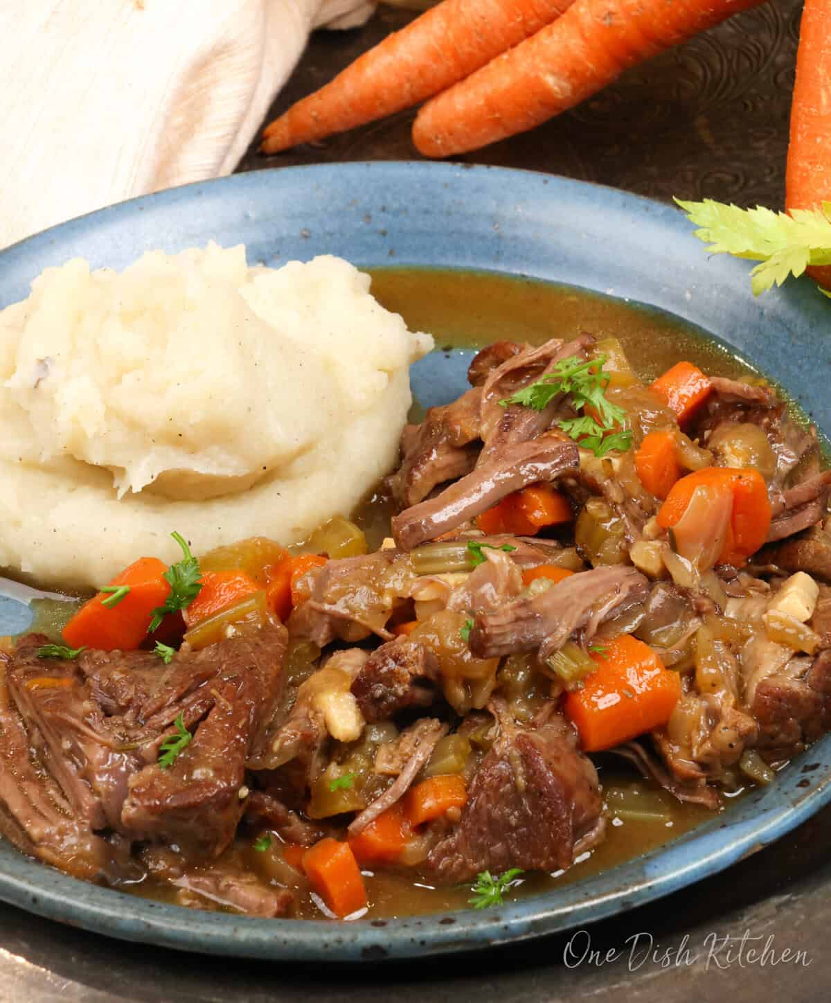 pot roast with vegetables alongside mashed potatoes on a blue plate.