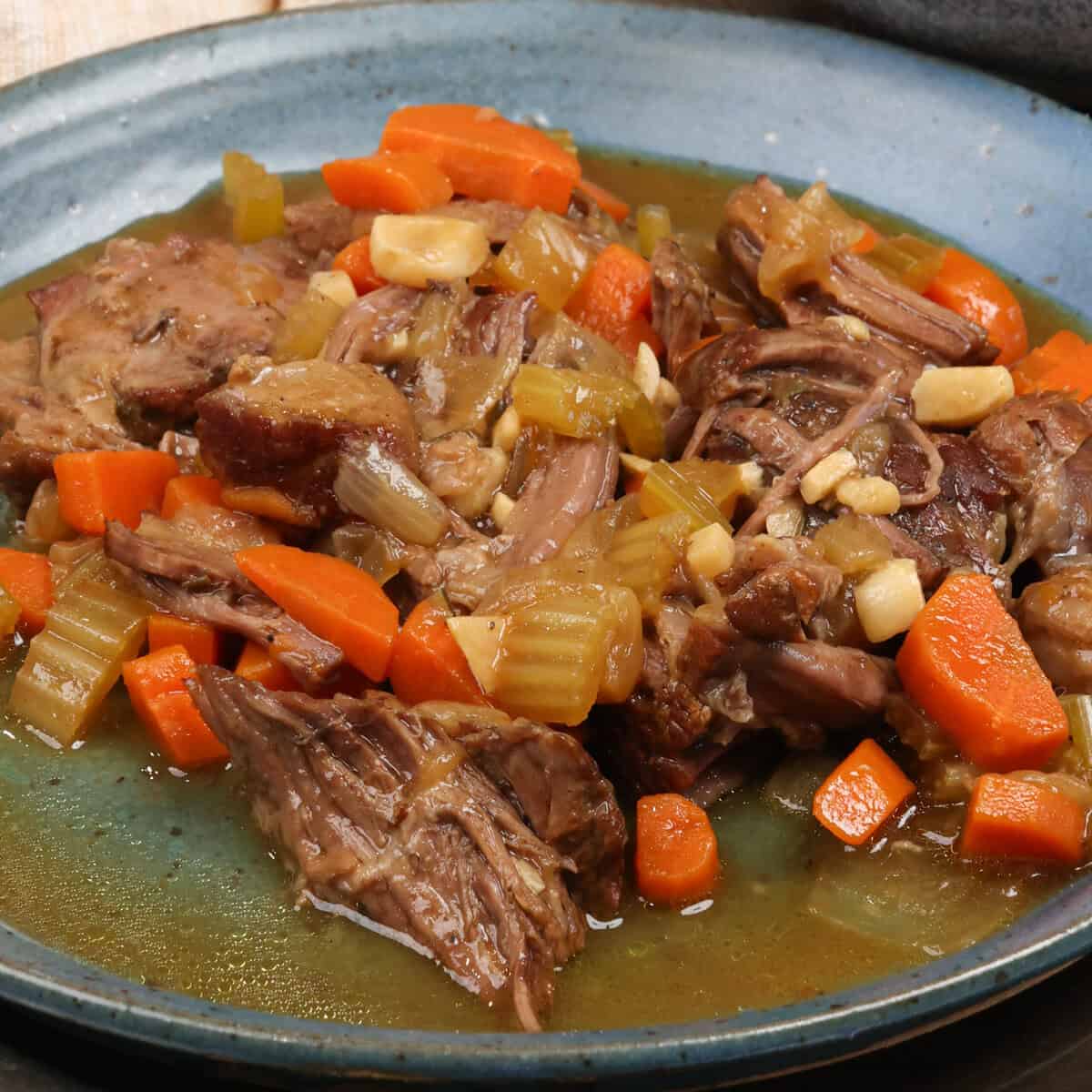 cooked chuck roast on a plate with gravy and carrots.