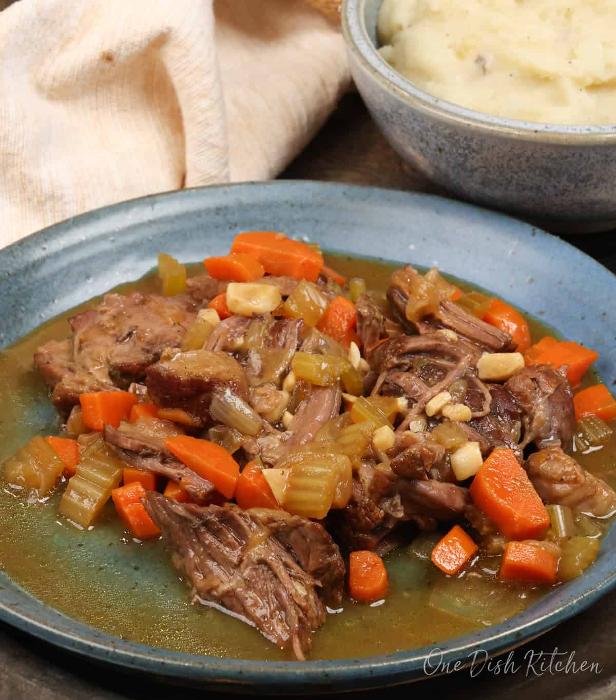 pot roast with vegetables on a plate next to a bowl of mashed potatoes.