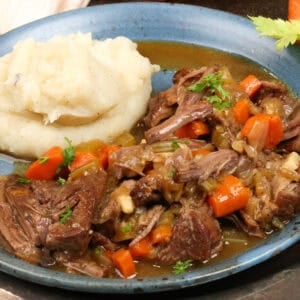 pot roast with vegetables alongside mashed potatoes on a blue plate.