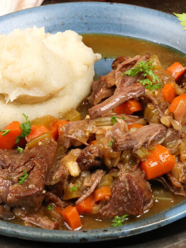 pot roast with vegetables alongside mashed potatoes on a blue plate.