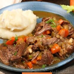 pot roast with vegetables alongside mashed potatoes on a blue plate.