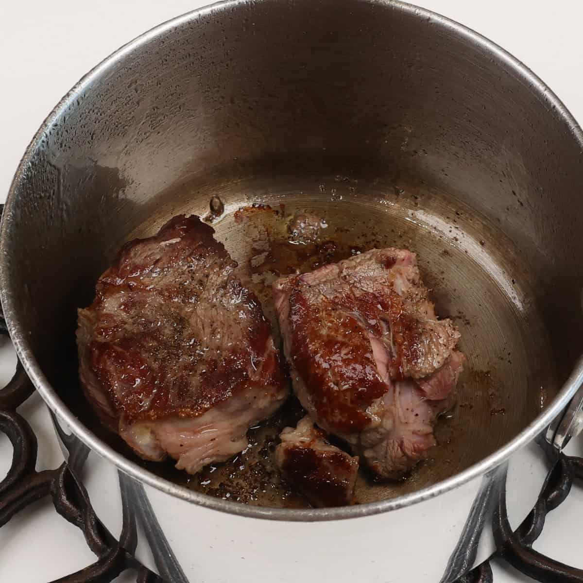 two pieces of chuck roast browning in a small pot.