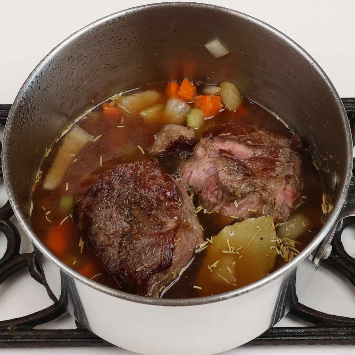 pot roast covered with broth and vegetables in a pot.