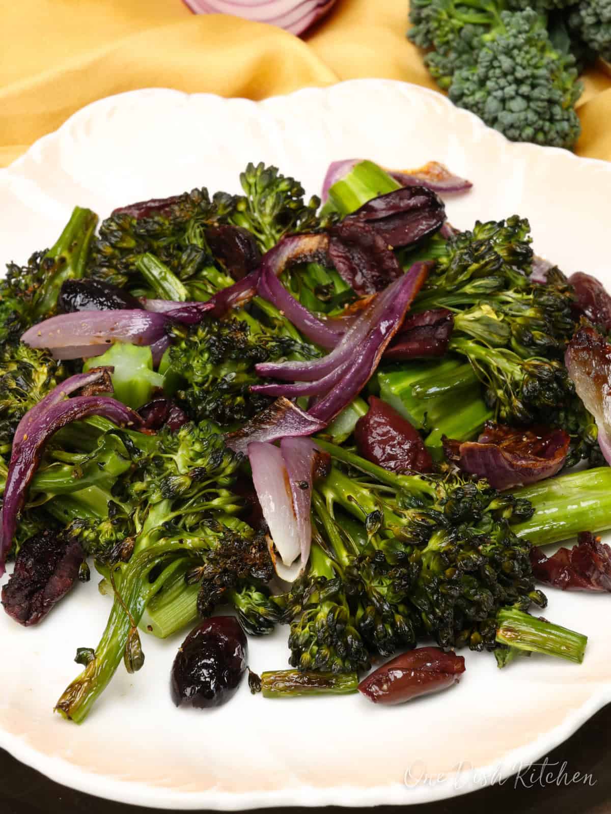 charred broccolini on a plate with red onions and kalamata olives.