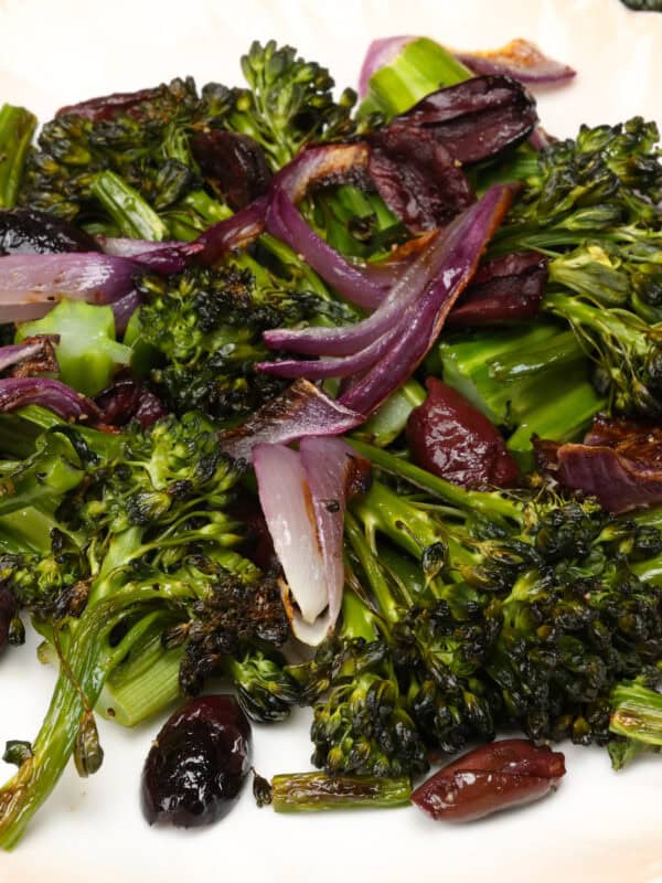 charred broccolini on a plate with red onions and kalamata olives.