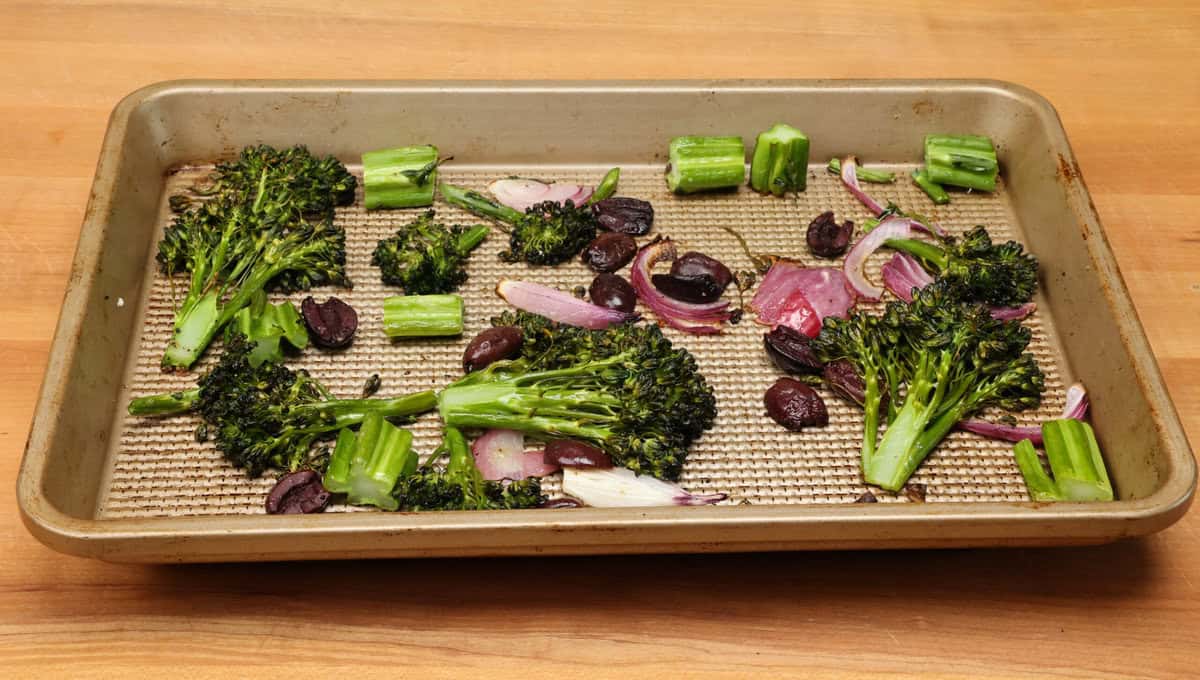 broccolini roasted on a baking sheet with olives and onions scattered around.