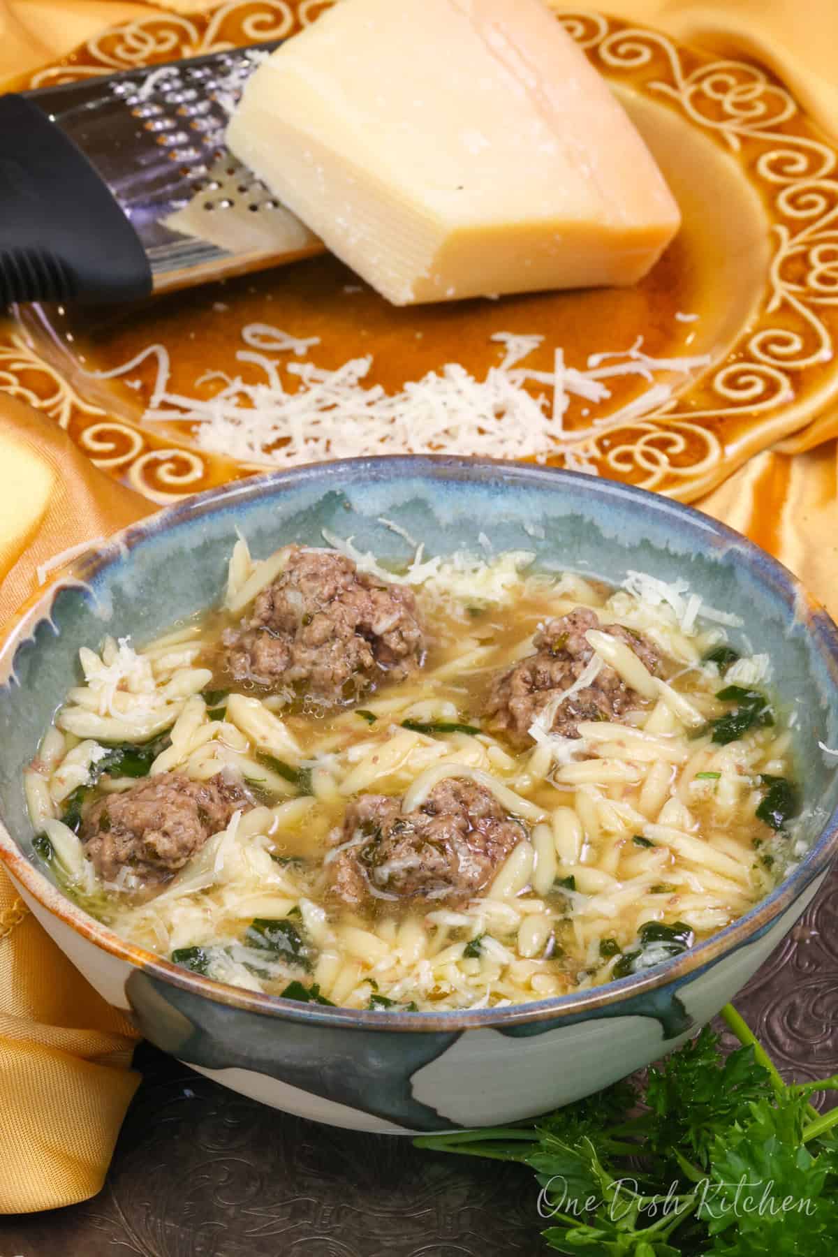 a bowl of Italian Wedding Soup next to a plate of fresh Parmesan cheese.