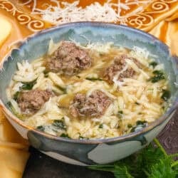 a bowl of Italian Wedding Soup next to a plate of fresh Parmesan cheese.