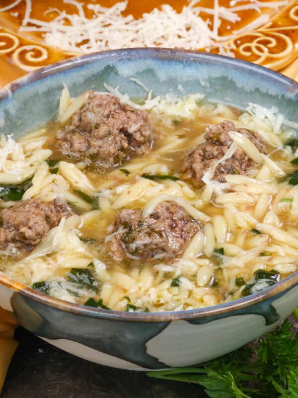 a bowl of Italian Wedding Soup next to a plate of fresh Parmesan cheese.