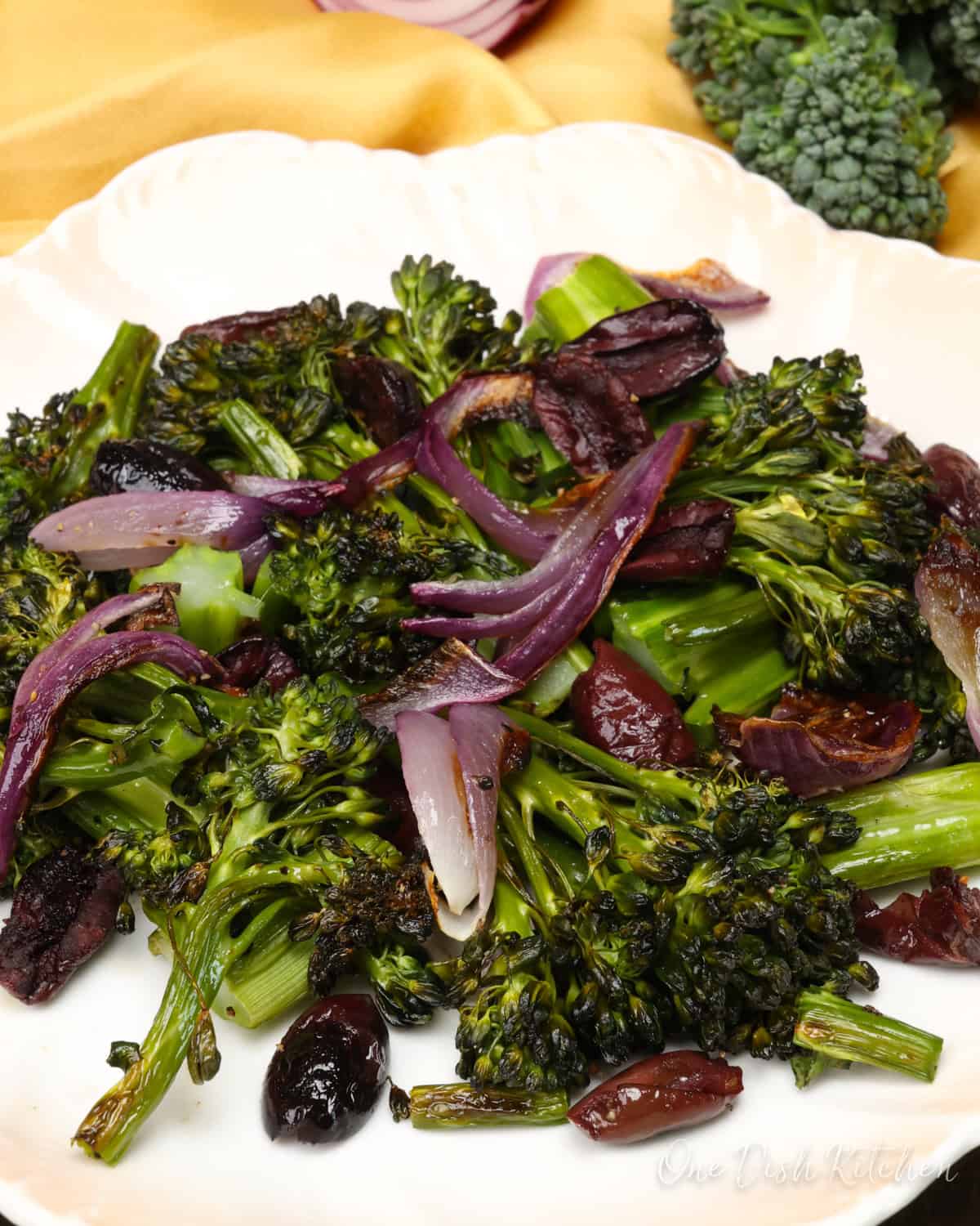 charred broccolini on a plate with red onions and kalamata olives.