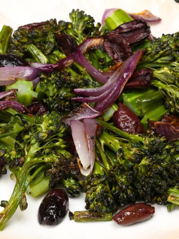 charred broccolini on a plate with red onions and kalamata olives.