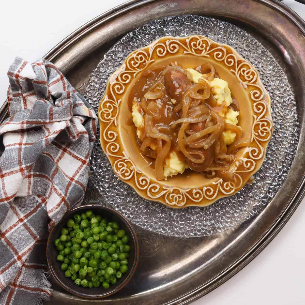 an overhead view of bangers and mash on a silver tray.