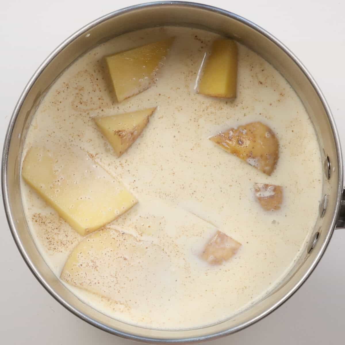 cubed potatoes in a saucepan covered by milk and cream.