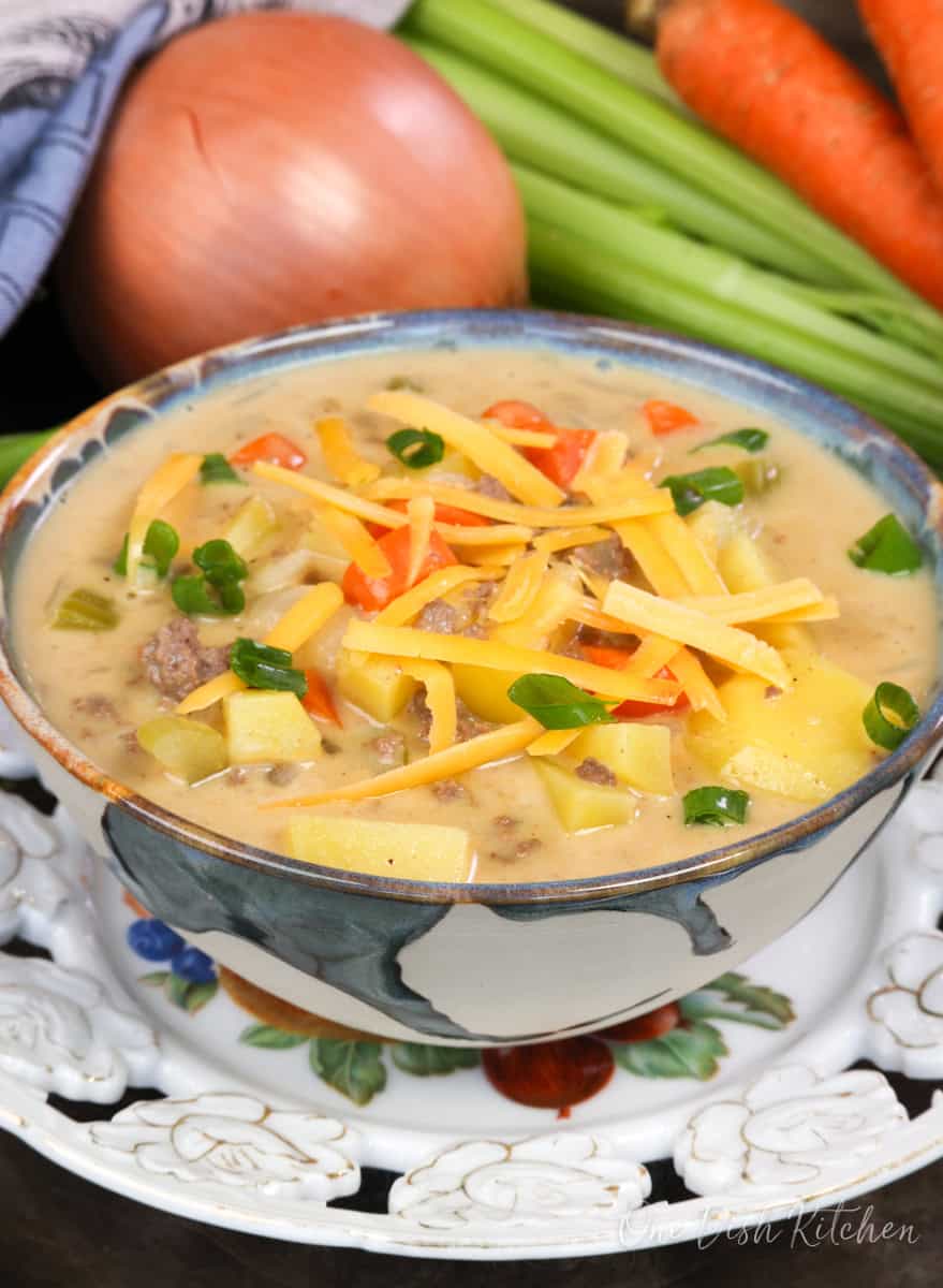 a bowl of cheeseburger soup topped with fresh shredded cheese and sliced green onions.