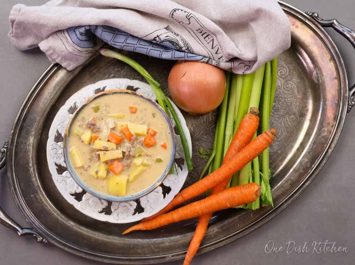 a bowl of cheeseburger soup on a silver tray next to a grey napkin.