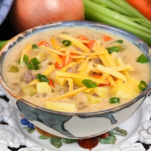 a bowl of cheeseburger soup topped with fresh shredded cheese and sliced green onions.