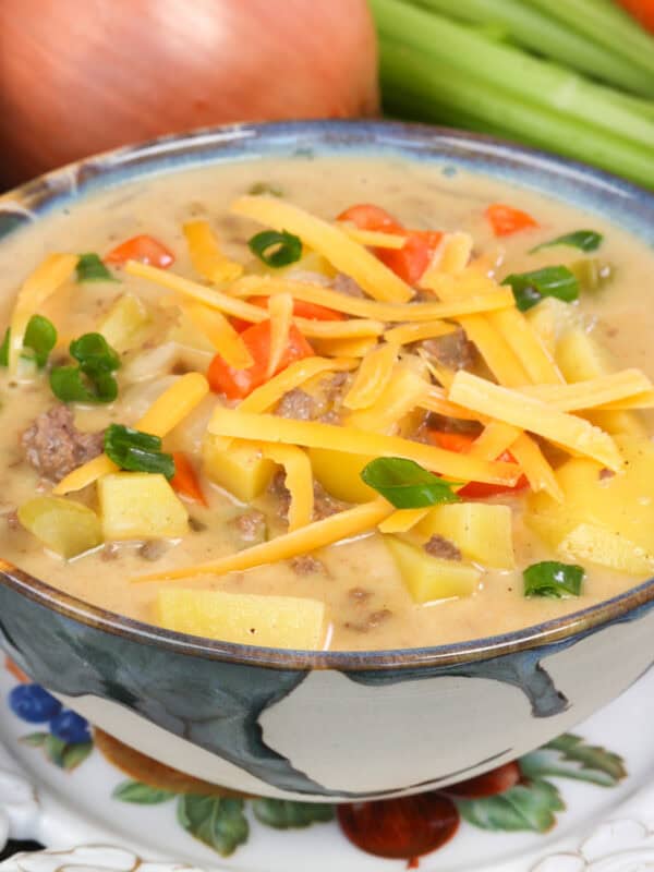 a bowl of cheeseburger soup topped with fresh shredded cheese and sliced green onions.