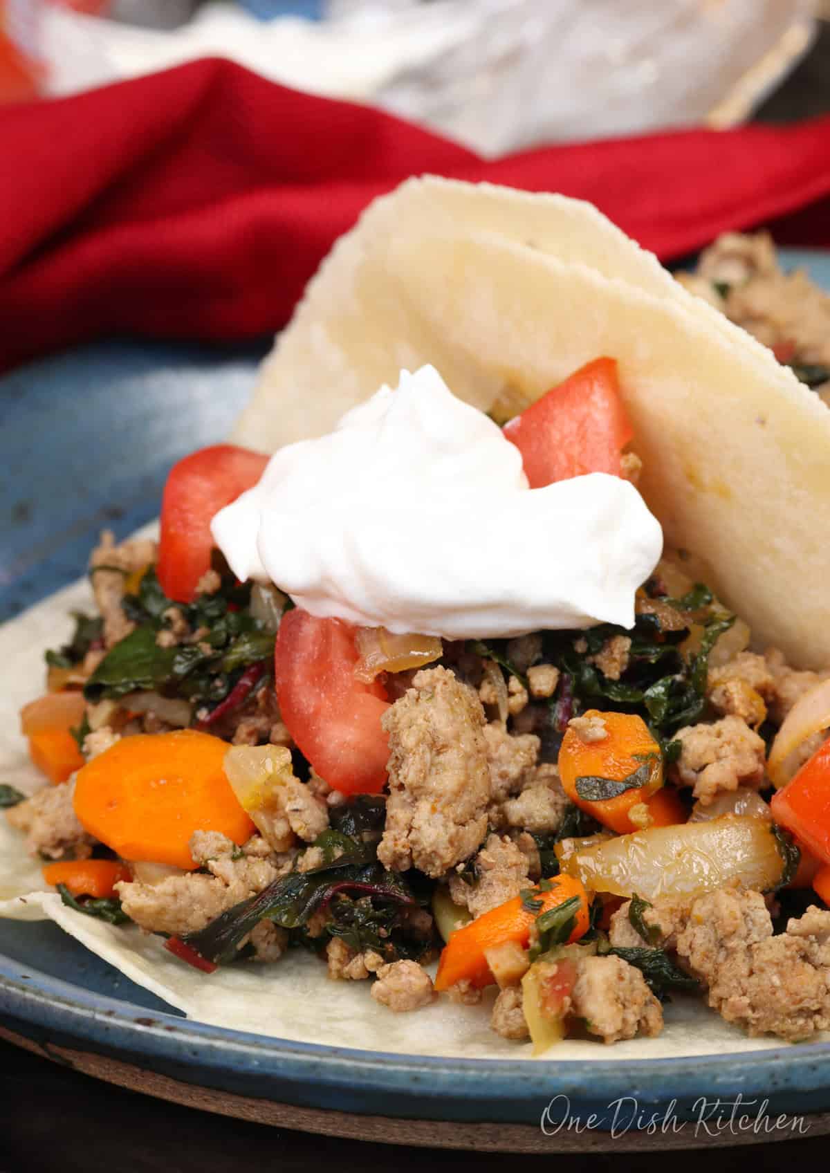 a tortilla filled with ground turkey and vegetables and topped with sour cream on a blue plate.