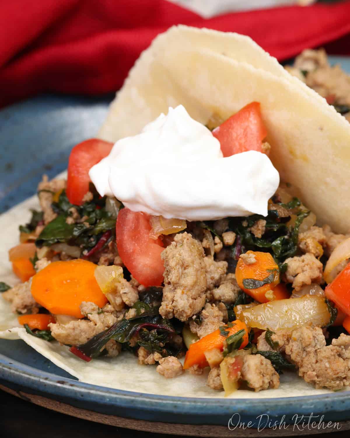 a tortilla filled with ground turkey and vegetables and topped with sour cream on a blue plate.