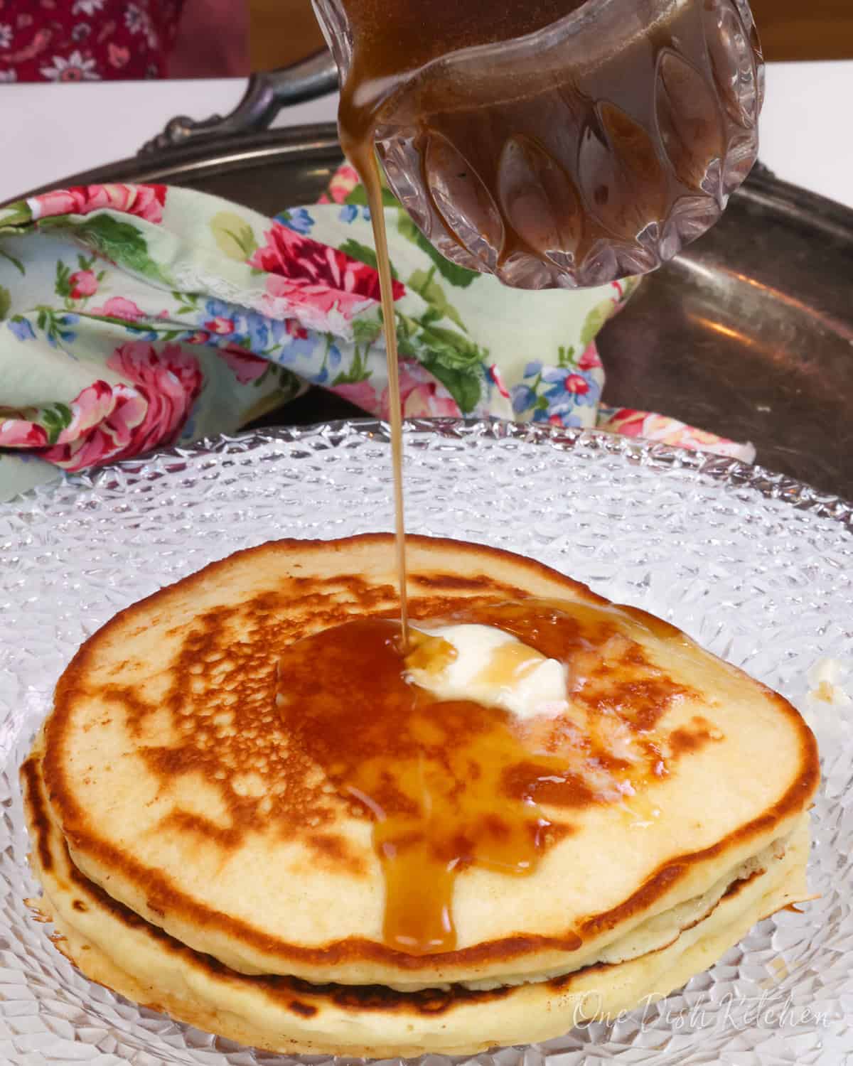 pancakes on a white plate with pancake syrup poured over the top.