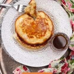 a stack of pancakes on a plate with syrup being poured over the top.