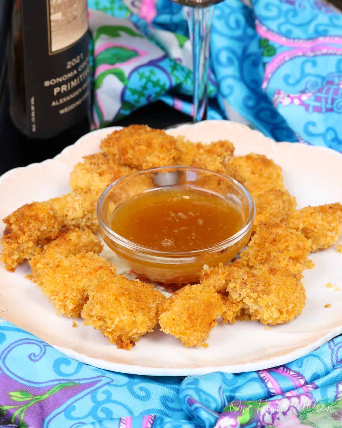 popcorn chicken on a white plate with a bowl of sauce in the center.