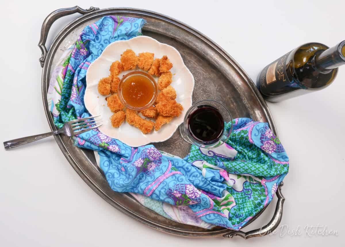 popcorn chicken on a silver tray with a glass of wine and a blue napkin.