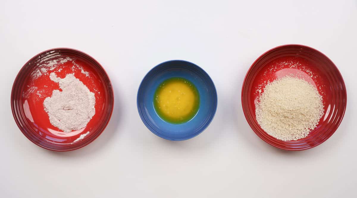 a bowl of flour, next to a bowl of melted butter, next to a bowl of breadcrumbs on a table.