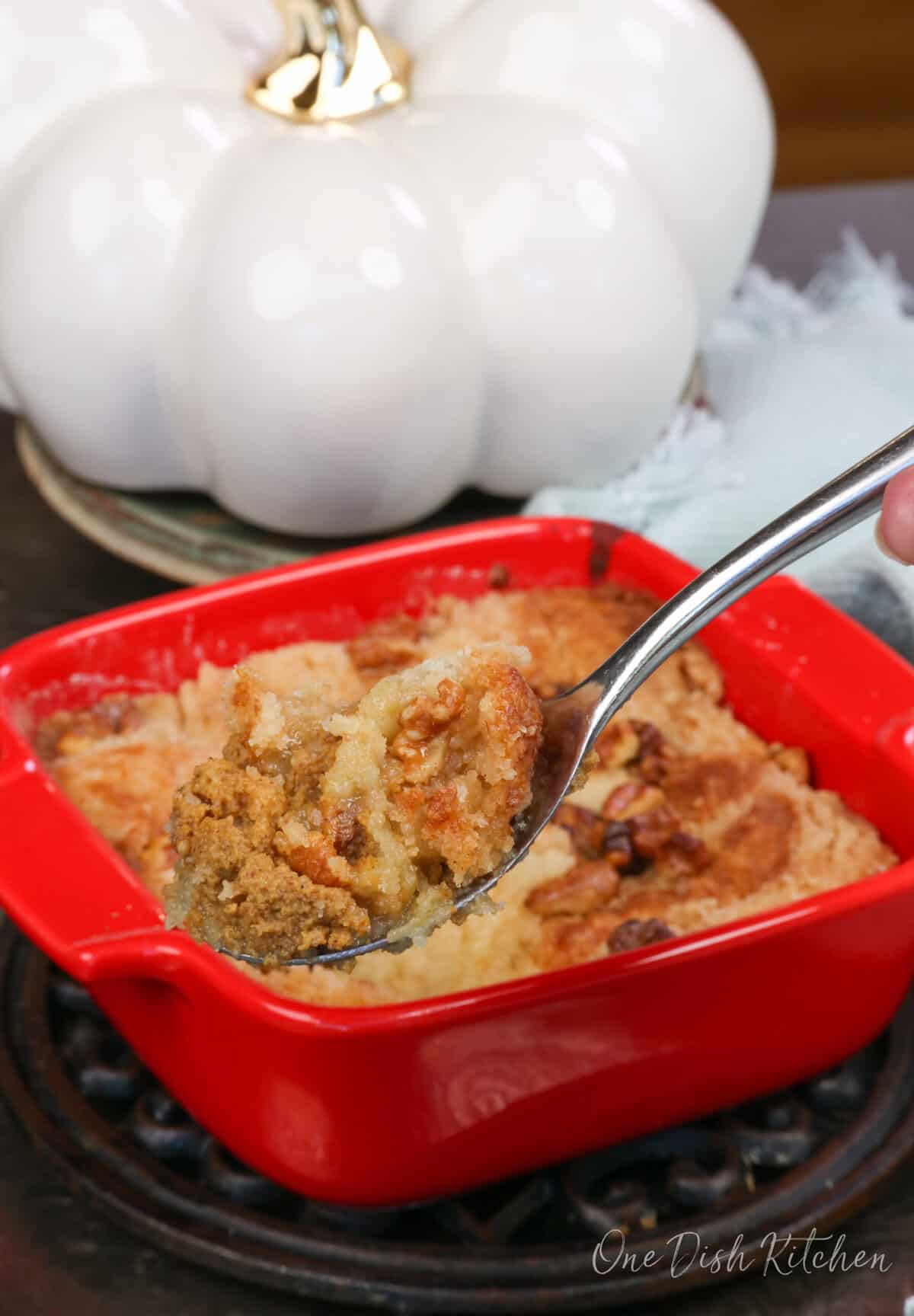 a small pumpkin dump cake in a square red baking dish with a spoon on the side.