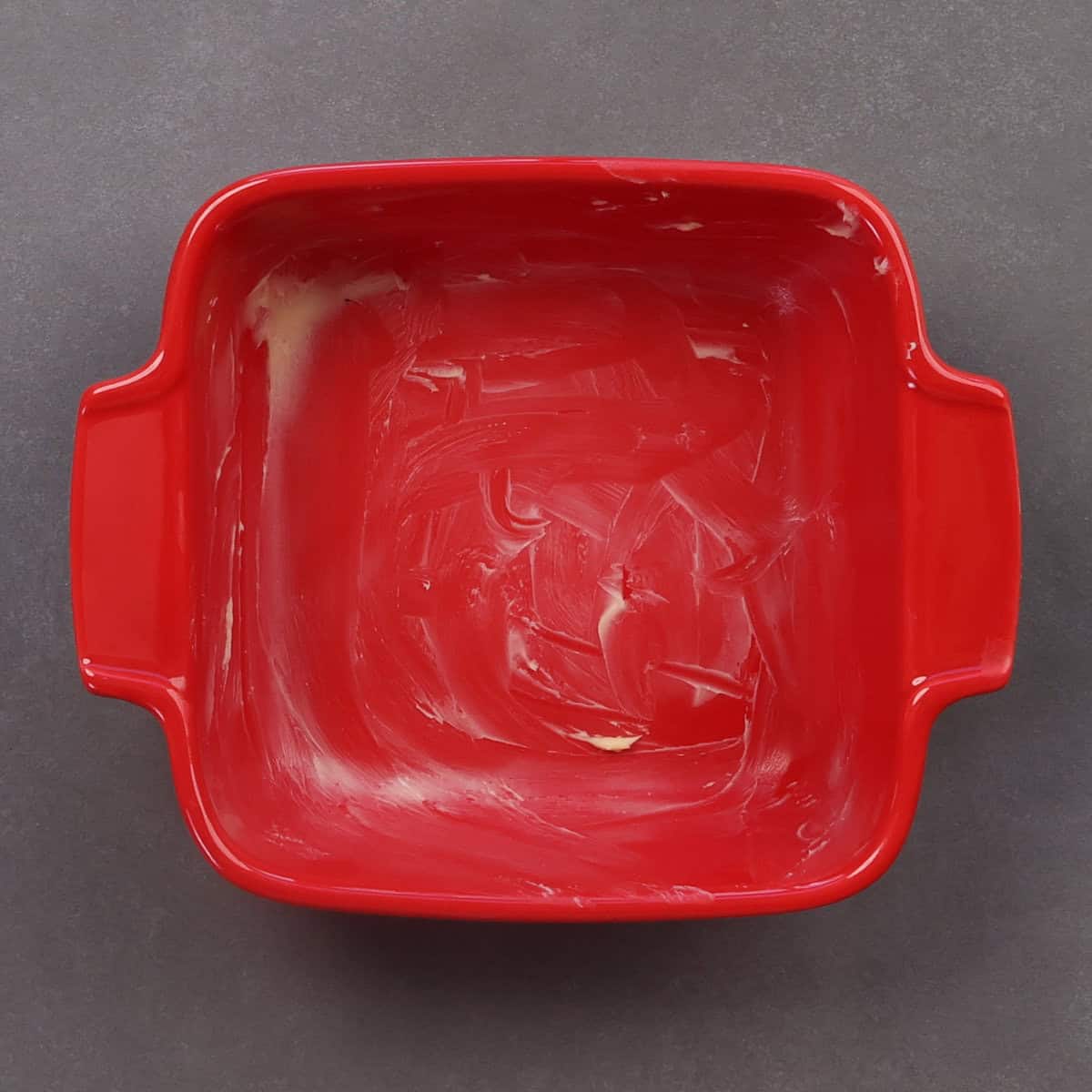 a small red buttered baking dish on a gray table.