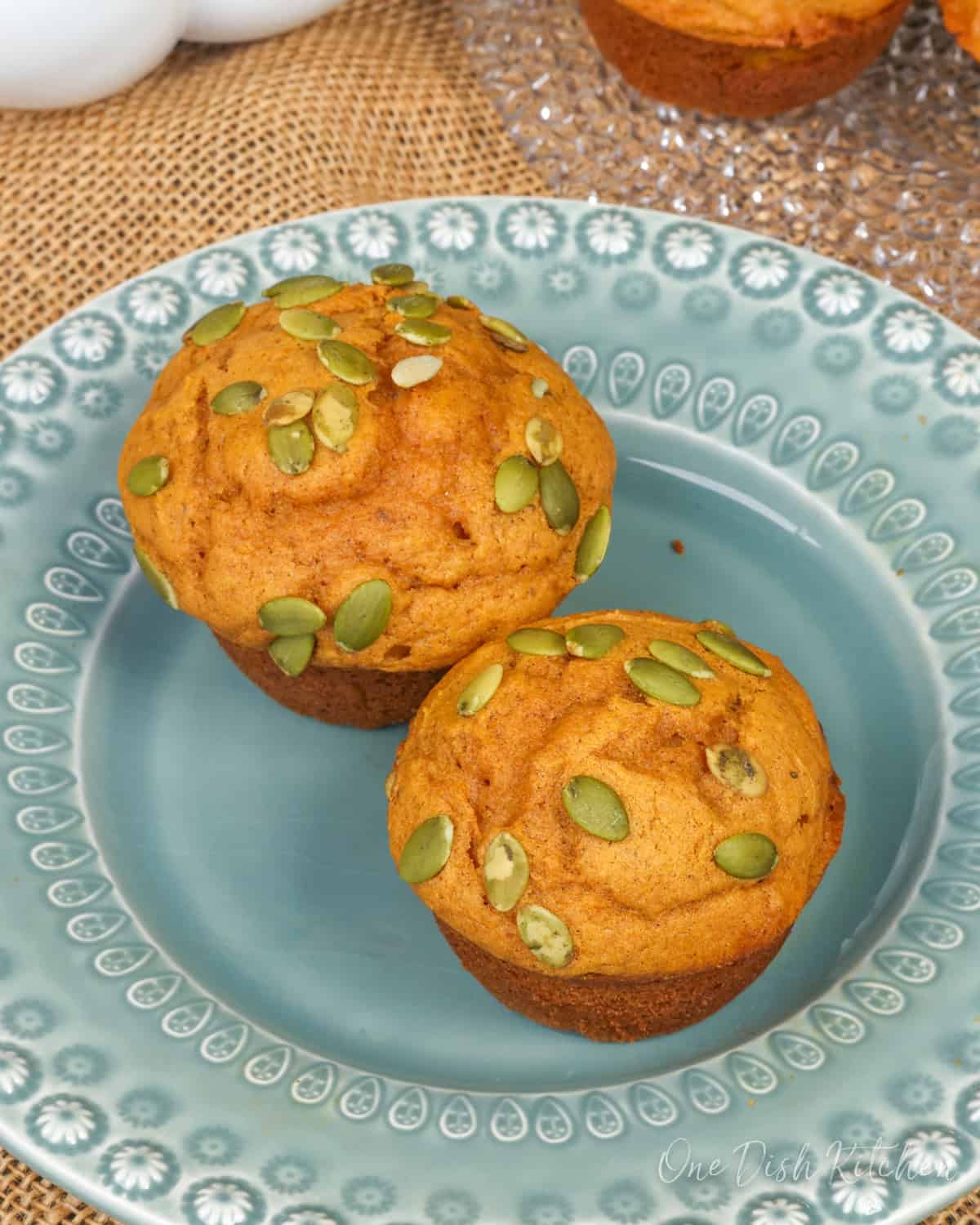 two pumpkin muffins topped with pumpkin seeds on a green plate.