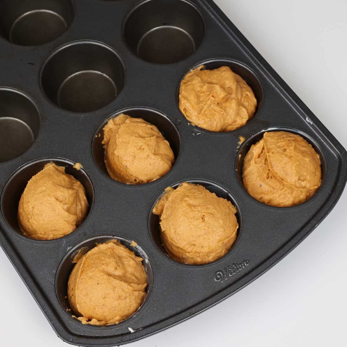 six unbaked pumpkin muffins in a muffin tin.