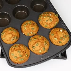 Six pumpkin muffins topped with pumpkin seeds.