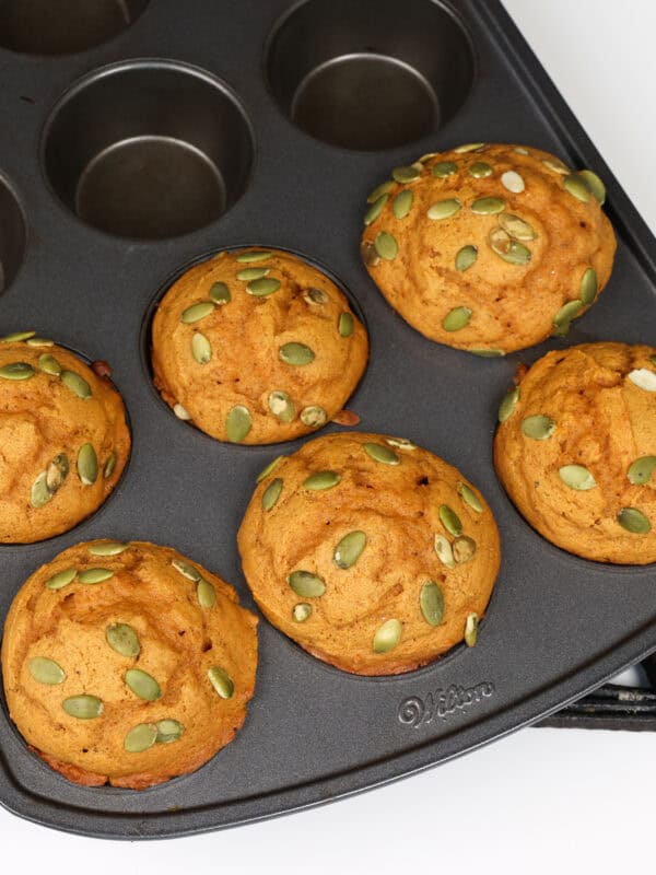 Six pumpkin muffins topped with pumpkin seeds.