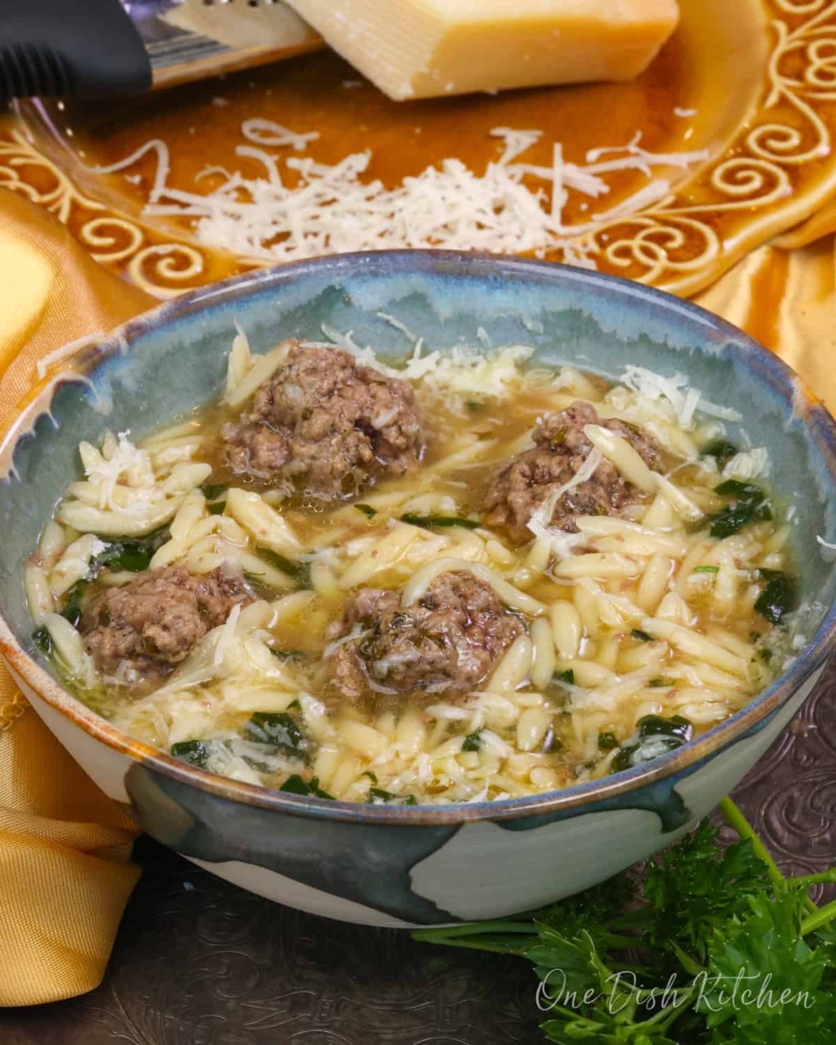 a bowl of Italian Wedding Soup next to a plate of fresh Parmesan cheese.