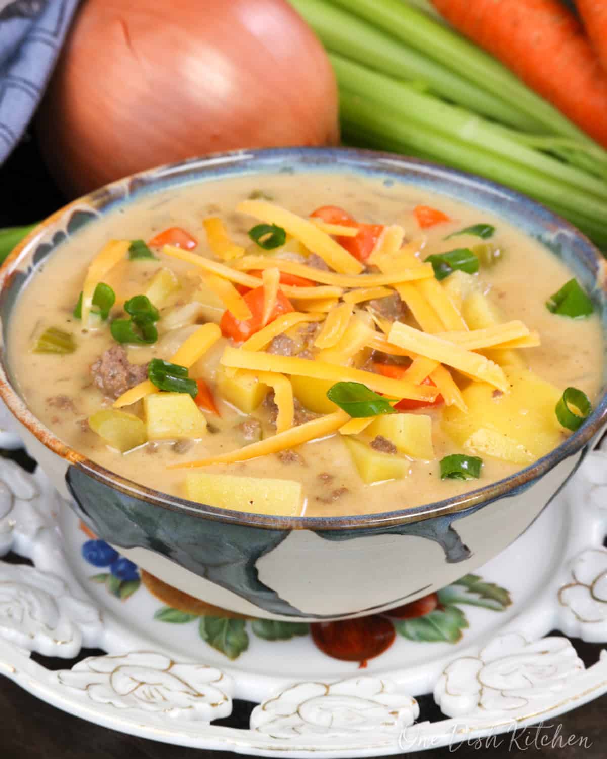 a bowl of cheeseburger soup topped with fresh shredded cheese and sliced green onions.