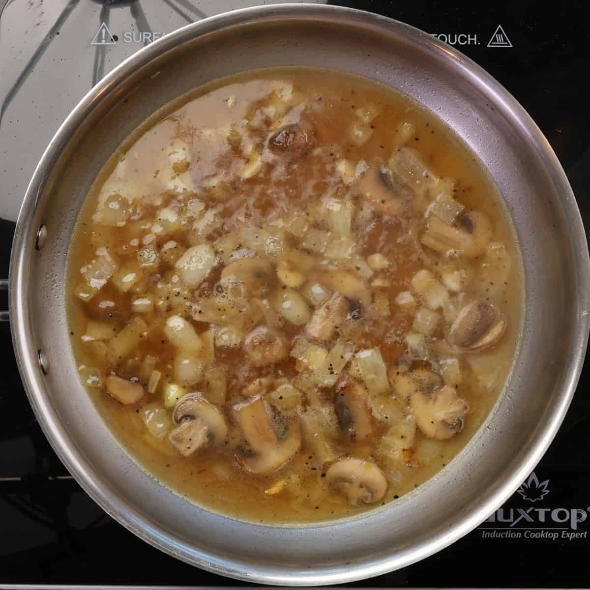 mushrooms, onions, and broth simmering in a skillet.