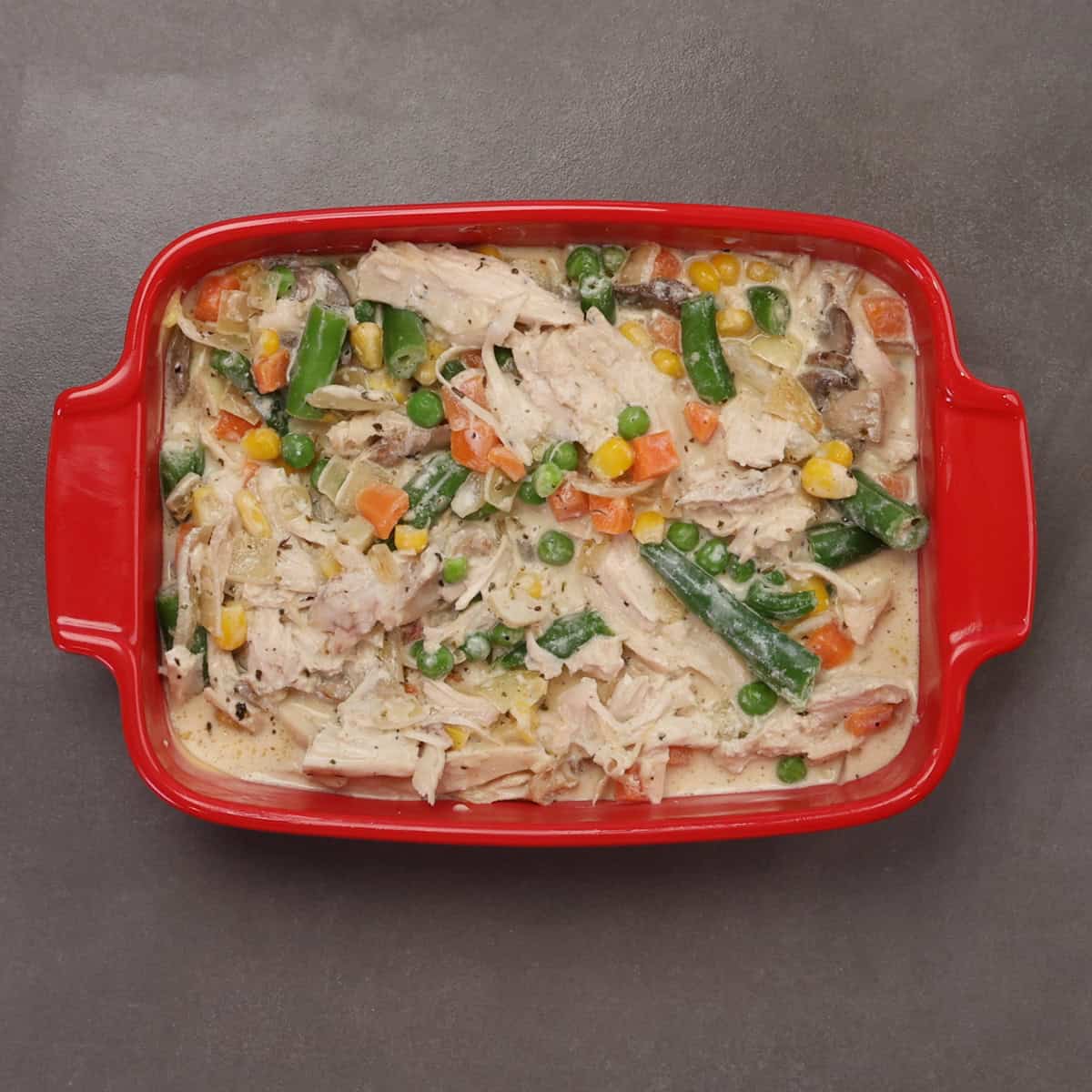 unbaked chicken casserole in a small red baking dish.